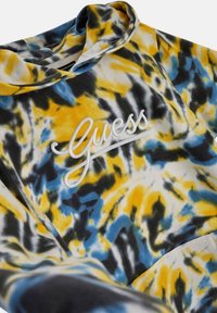 Hoodie mit einem Batikmuster in Gelb-, Blau- und Schwarztönen, akzentuiert durch ein gesticktes „Guess“-Logo in Weiß. Weicher Stoff.