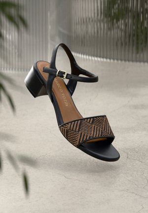 Sandal à talon en cuir noir avec une sangle tissée à motif marron et noir. Caractéristiques : boucle à la cheville et semelle beige. Design de talon carré.