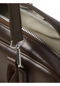 Braune Ledertasche mit offenem silberfarbenem Reißverschluss, der das beige Fischgrätfutter zeigt, und angebrachtem Lederriemen mit Metallverschluss.