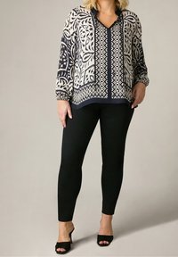 Långärmad blus i krämfärg och marinblå med djärva tryckta mönster och v-ringning, kombinerad med figurnära svarta leggings och svarta klackskor.