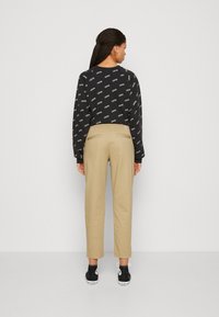 Maglietta nera a maniche lunghe con motivo logo bianco, pantaloni khaki a gamba affusolata e sneakers nere con suola bianca. Design semplice e informale.