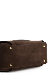 Sac à main en daim marron avec des clous métalliques dorés et un fond plat. Équipé de poignées arrondies et d'une surface lisse et texturée. Design minimaliste.
