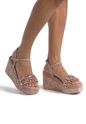 Sandalias de cuña en material rosa suave con suela de esparto texturizada. Presentan una tira decorada con joyas con acentos transparentes y en tonos rosados.