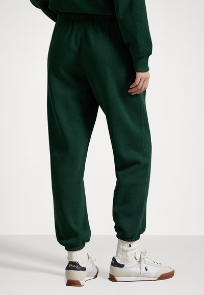 Dark green sweatpants with a tapered fit, elastic waistband, and cuffs. Paired with white sneakers and ribbed socks.