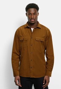 Braunes Langarmhemd aus strukturiertem Stoff mit zwei Brusttaschen und Knopfverschluss. Verfügt über einen geraden Schnitt und einen spitzen Kragen.