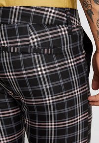 Svarta rutiga byxor med ett flerfärgat mönster av rosa och grå linjer. Inkluderar en bakficka och ett mjukt, texturerat tyg.