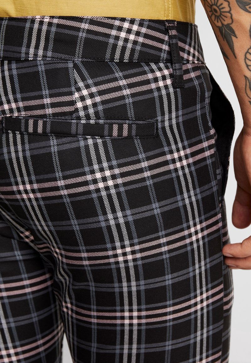 Svarta rutiga byxor med ett flerfärgat mönster av rosa och grå linjer. Inkluderar en bakficka och ett mjukt, texturerat tyg.