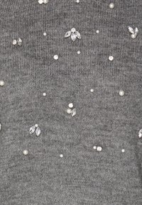 Grauer Strickpullover mit verstreuten Verzierungen, darunter Perlen und Strasssteine, der eine strukturierte Stoffqualität und verschiedene Dekorationsmuster aufweist.
