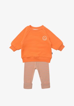 Orange sweatshirt with a front smiley face print, paired with light gray and orange striped leggings. Soft cotton material, casual design.