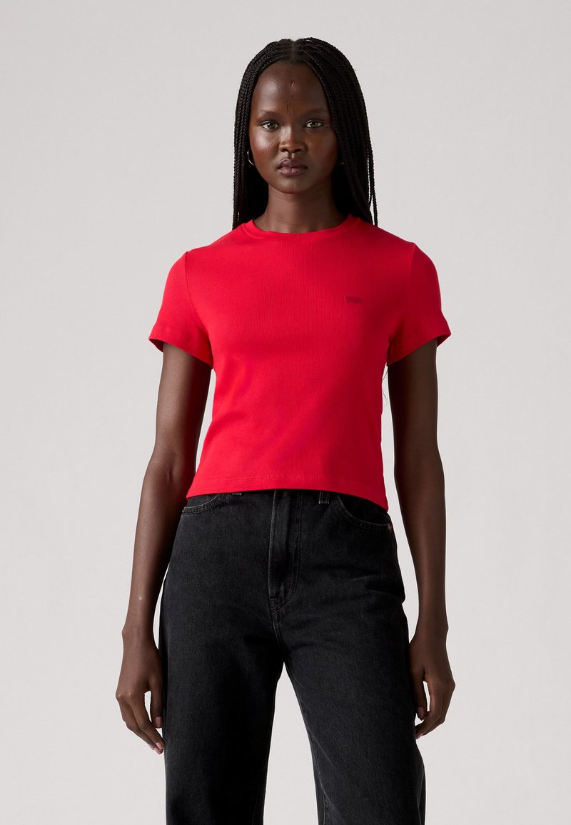 T-shirt rouge à manches courtes côtelé avec un col rond et un petit logo de marque. Associé à un jean noir taille haute pour un look court.
