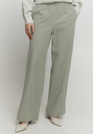 Light green, wide-leg pants with an elastic waistband. Soft fabric with a smooth texture. Paired with beige, pointed-toe shoes.