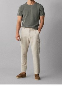Maglietta grigia a righe con maniche corte, pantaloni cargo beige con tasche laterali, scarpe slip-on in tessuto intrecciato color sabbia, design minimale, texture del tessuto liscia.