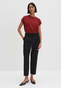 T-shirt rosso a maniche corte abbinato a pantaloni neri su misura. I pantaloni hanno una vestibilità dritta e una linea piatta. Il modello indossa mule nere.