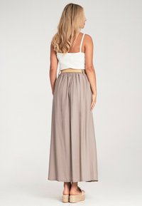 Maxi-Rock aus hellgrauem Stoff mit einem elastischen Bund, der bis zu den Knöcheln fällt. Kombiniert mit einem weißen Crop-Top und beigen Plateausandalen.