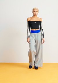 Musta lyhyt crop-top, jossa on pitkät raidoitetut hihat, harmaat leveälahkeiset collegehousut, joissa on sininen joustovyötärö, yhdistetty tummiin kenkiin keltaisella lattialla.