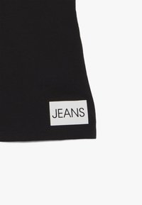 Czarne dżinsy wykonane z denimu, z białą prostokątną metka, na której widnieje wyraz "JEANS" wydrukowany pogrubionymi czarnymi literami.