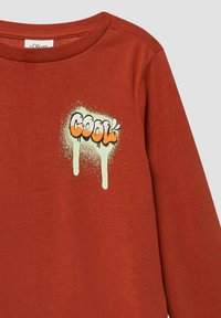 Rdzawoczerwony longsleeve z graffiti-style napisem "Cool" w pomarańczowym i białym kolorze z efektem spływającej farby na klatce piersiowej.
