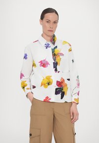 Floral-patterned shirt with a white base, featuring colorful flowers in pink, yellow, and purple. Button-up design and long sleeves.