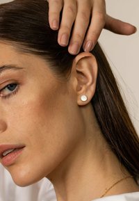 Runde Metall-Streifenohrstecker aus Gold mit einer glatten, glänzenden Oberfläche. Nahaufnahme eines Ohrs und einer Hand, die das Design der Ohrringe hervorhebt.