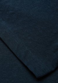 Námorně modrý textil s texturovaným povrchem, s viditelnými stehy podél okrajů, vytvářející vrstvený vzhled.