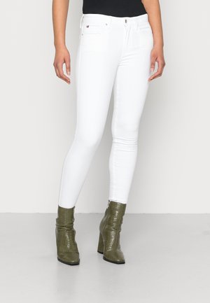 Jeans skinny bianchi con vita media, dotati di tasche e ferramenta argento, abbinati a stivaletti texani verde oliva.