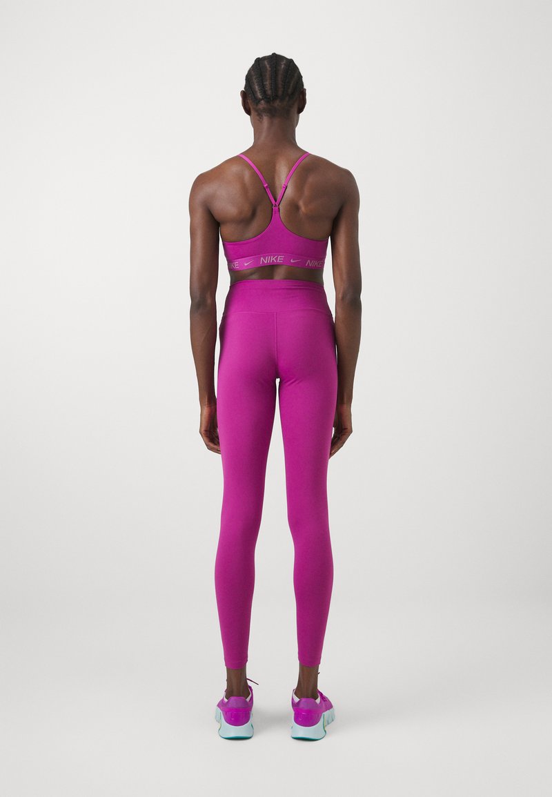 Sostenedor deportivo fucsia con tirantes finos y logotipo, combinado con leggins de talle alto a juego. Los zapatos tienen una suela azul y detalles en rosa.