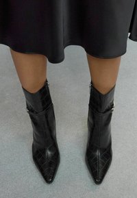 Bottines noires en simili cuir avec une texture crocodile, bout pointu et zips décoratifs sur les côtés extérieurs.