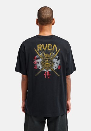 Personne portant un T-shirt noir avec un casque de samouraï doré, des épées croisées et des caractères japonais rouges dans le dos sur un fond blanc.