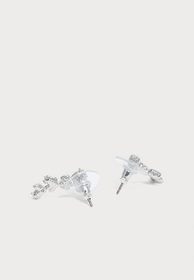 Paire de boucles d'oreilles en argent avec attaches en plastique transparent sur un fond clair uni.