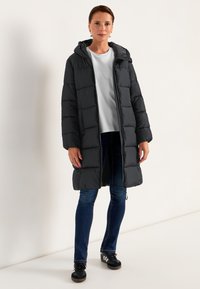 Svart puffjacka med huva, som har ett quiltat mönster, hel frontdragkedja och sidfickor. Kombinerad med jeans och svarta sneakers.
