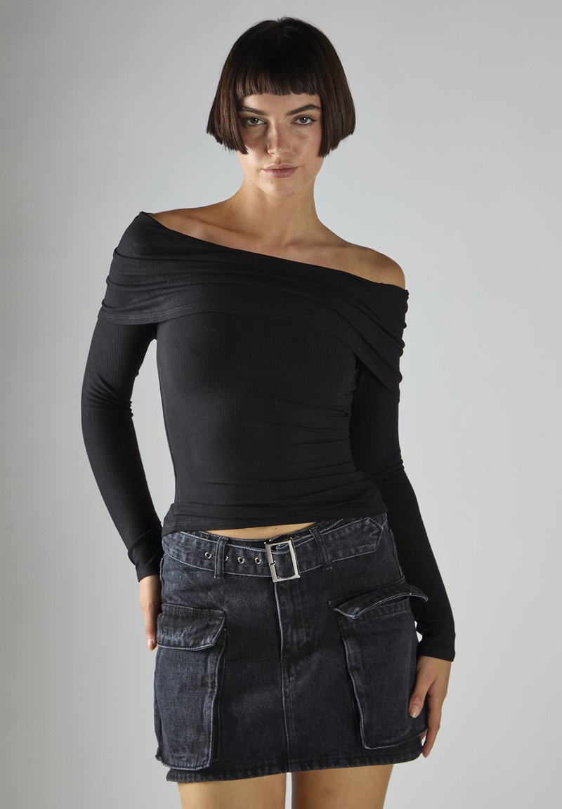 Top nero a maniche lunghe con scollo a barca e texture a coste, abbinato a una minigonna di denim scuro con tasche frontali e fibbia metallica alla cintura.