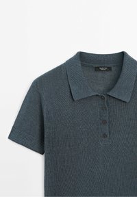Polo en maille gris foncé à manches courtes avec col et quatre boutons sur la patte de boutonnage avant, plié à plat sur fond blanc.
