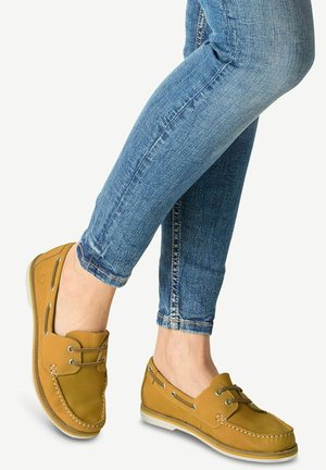 Tan boot schoenen met een gestructureerde bovenkant, decoratieve veters en een contrasterende witte rubberen zool, gestyled met blauwe slim-fit jeans.