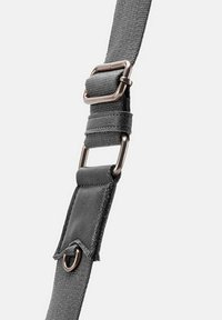 Grau gespannter Stoffriemen mit strukturiertem Finish, ausgestattet mit einer Metallschnalle und Lederdetails. Enthält einen runden Metallbefestigungspunkt.