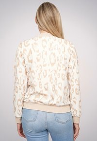 Bluza w panterkę w jasnym beżu z teksturowanym wzorem, ściągaczami przy mankietach i dolnym obszyciu. Połączona z jasnoniebieskimi dżinsami.