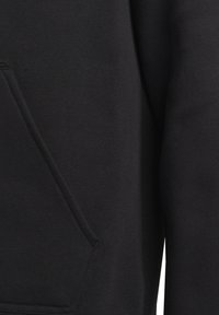 Gros plan sur un tissu noir avec une poche diagonale et des coutures visibles sur la manche et le corps d'un vêtement.