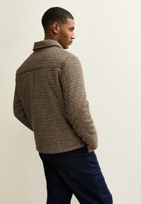 Chaqueta a cuadros marrón y crema con cuello, fabricada con un tejido texturizado y de corte relajado, combinada con pantalones de mezclilla oscuros.