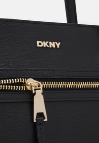 Black handbag made of textured synthetic material, featuring a gold zip closure and a gold DKNY logo. Notable hardware includes a gold zipper pull.