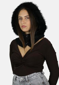 Cappuccio in ecopelliccia nera con colletto aderente e dettagli a bottone, abbinato a una maglia marrone con scollatura a V profonda e jeans a vita alta grigio chiaro.