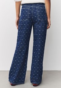 Szerokie dżinsy z ciemnoniebieskiego denimu z białymi wzorami w kokardki, pięciokieszeniowe, z subtelnymi detalami szwów na tylnej kieszeni.