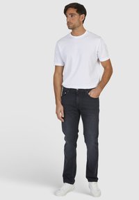 Ciemnoniebieskie dżinsy o slim fit, z przednimi kieszeniami i widocznym szwem. W zestawieniu z gładką białą koszulką i białymi sneakersami.