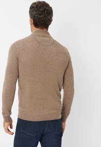 Brauner Strickpullover mit hohem Kragen, gerippten Bündchen und Saum. Hat eine strukturierte Oberfläche mit dezenten Sprenkeln. Getragen mit dunklen blauen Jeans.