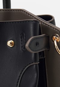 Närbild av en svart och olivgrön läderaxelväska med guldiga detaljer, sömnadsdetaljer och en distinkt texturerad finish.