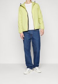 Jasnozielona kurtka na suwak z regulowanym kapturem, w połączeniu z białym t-shirtem i niebieskimi jeansami o prostych nogawkach. Dopełnieniem stroju są białe trampki.