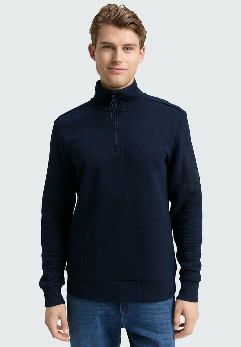 Sudadera con cremallera en color navy, con tejido texturizado, cuello alto y puños acanalados. Presenta un detalle en el hombro y un dobladillo recto.