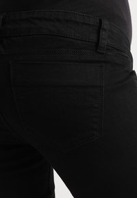 Jeans in denim nera con una texture liscia, dotati di una tasca posteriore e cuciture doppie lungo le cuciture per un tocco di dettaglio.
