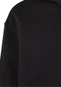 Gros plan d'un tissu noir uni montrant la couture d'épaule et une partie de la manche longue sur un vêtement textile.