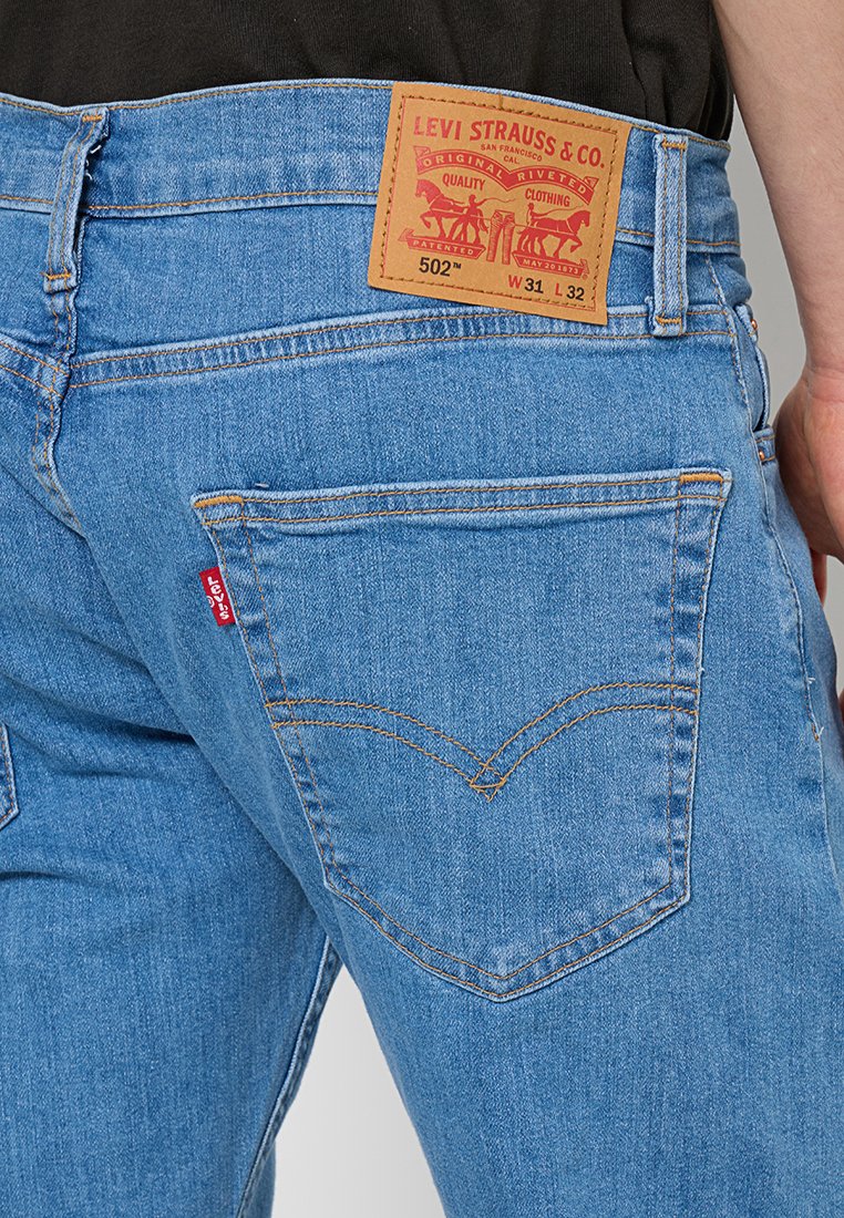 Jean Levi's 502 en denim bleu clair, avec une patch en cuir portant la marque, coupe droite et couture distinctive sur les poches arrière.