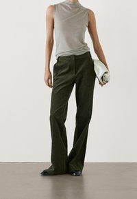 Haut sans manches gris clair associé à un pantalon large vert foncé. Le tissu a une texture douce, complétée par une pochette blanche et des chaussures noires.