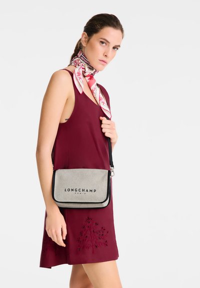 Graue Longchamp Umhängetasche mit schwarzem Besatz, die den Markennamen deutlich in Schwarz zeigt. Mit glatter Textur und rechteckiger Form.